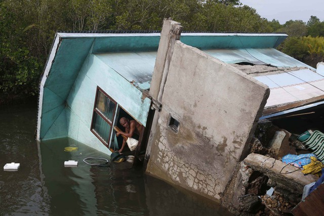 Một người đàn ông nhìn ra ngoài cửa sổ của ngôi nhà bị đổ xuống sông ở Bohol, Philippines.