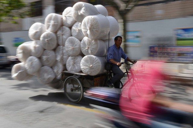 Một người đàn ông đạp xe ba bánh chở vật liệu bọc hàng ra chợ bán tại Thượng Hải, Trung Quốc.