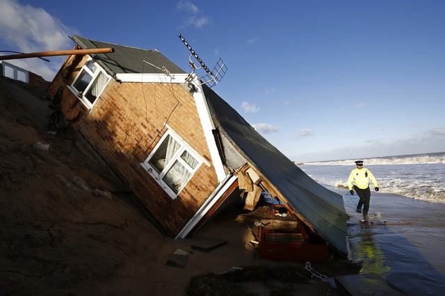 Một cảnh sát đi qua ngôi nhà rơi xuống biển do mưa bão gây sạt lở ở Hemsby, Anh.