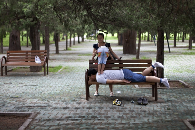 Một cậu bé đứng trên lưng bố đang nằm trên ghế trong một công viên ở Bắc Kinh, Trung Quốc.