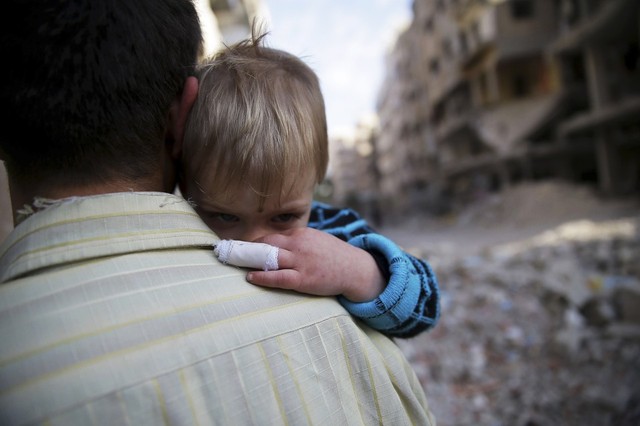 Một người đàn ông bế con nhỏ đi qua những ngôi nhà đổ nát tại thành phố Damascus, Syria.
