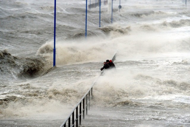 Mọi người ôm rào chắn khi sóng mạnh đánh vào một bến tàu tại bờ biển ở Dagebuell, Đức.