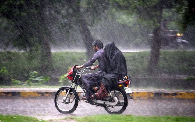 Một cặp đôi đi xe máy dưới mưa lớn ở Lahore, Pakistan.