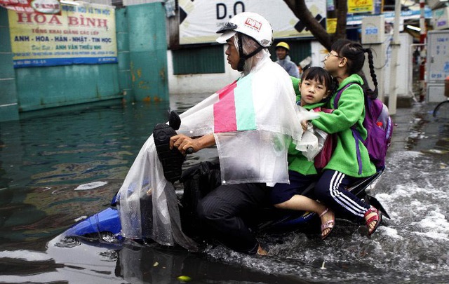 Một ông bố đi xe máy chở con tới trường qua đường phố ngập lụt ở thành phố Hồ Chí Minh, Việt Nam.