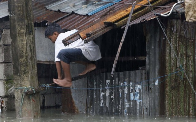 Một cậu bé trèo qua cửa sổ để lên mái nhà tránh nước lũ trên đường phố ở Quezon, Philippines.
