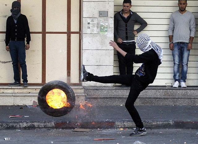 Một người Palestin đá chiếc lốp xe đang cháy về phía lực lượng an ninh Israel tại thành phố Hebron, Bờ Tây.
