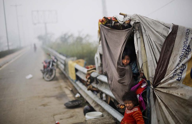Một bé gái vô gia cư thò đầu ra khỏi túp lều tạm ven đường trong sương sớm ở New Delhi, Ấn Độ.