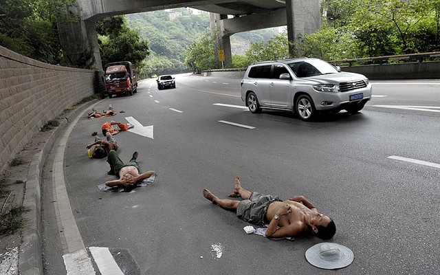 Người lao động nằm ngủ trên đường khi ô tô chạy qua ở thành phố Côn Minh, Trung Quốc.