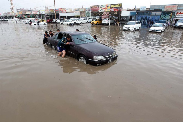 Trẻ em giúp đẩy một chiếc xe ô tô qua đường phố ngập lụt ở thành phố Baghdad, Iraq.