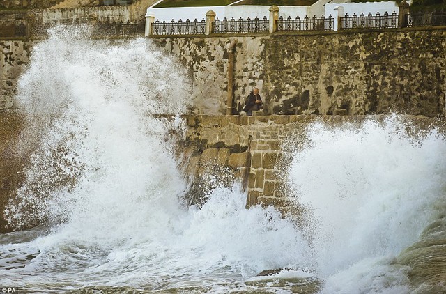 Quá gần cho thoải mái: Một người đàn ông nhìn vào một làn sóng rất lớn vì nó phá vỡ bên trong bến cảng ở Porthleven, Cornwall