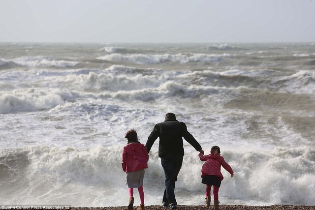 Cảm các yếu tố: Một người cha nắm tay con mình dọc theo bờ biển Sussex và sóng sụp đổ hoang dã vào bờ biển 