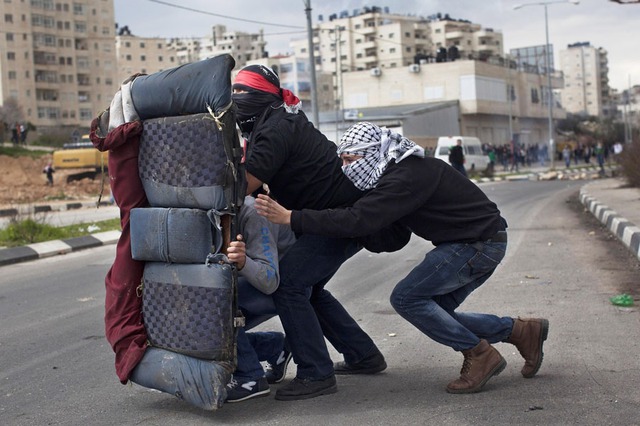 Người biểu tình Palestine che mặt sự dụng ghế sau của ô tô để che chắn trong khi đụng độ với quân đội Israel ở Ramallah, Bờ Tây.