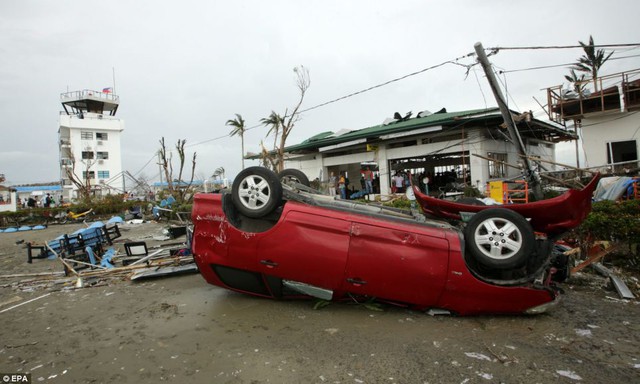 Ô tô bị gió thổi lật ngược, trong khi các ngôi nhà bị tàn phá nặng nề gần sân bay  tại thành phố Tacloban.