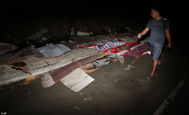 Một người dân đi qua những thi thể được che tạm bằng mái tôn tại thành phố Tacloban.