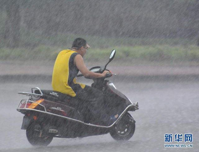 Một nam thanh niên đi xe dưới trời mưa lớn ở thành phố Quỳnh Hải, tỉnh Hải Nam.