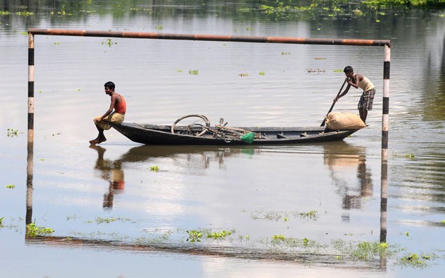 Người dân chèo thuyền qua một sân bóng đá bị ngập nước ở ngôi làng Mukata, Ấn Độ.