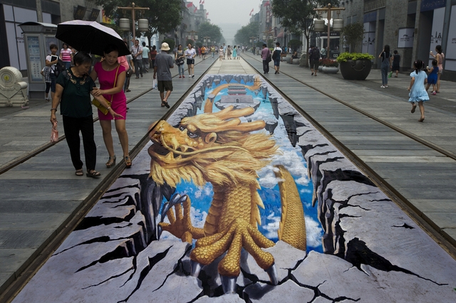 Mọi người đi qua một bức trang rồng vẽ bằng công nghệ 3D trên đường phố Qianmen ở Bắc Kinh, Trung Quốc.