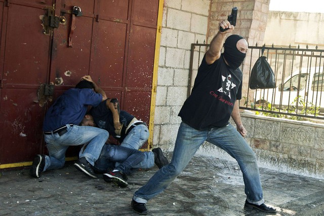 Một cảnh sát Israel cầm súng trong khi những đồng đội khác bắt giữ một người biểu tình Palestin tại Đông Jerusalem.