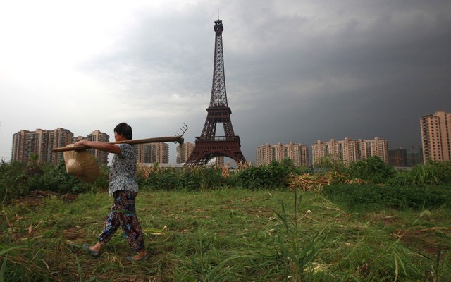 Một người nông dân vác cào đi qua tháp Eiffel mô phỏng tại khu đô thị Tianducheng ở thành phố Hàng Châu, tỉnh Chiết Giang, Trung Quốc.