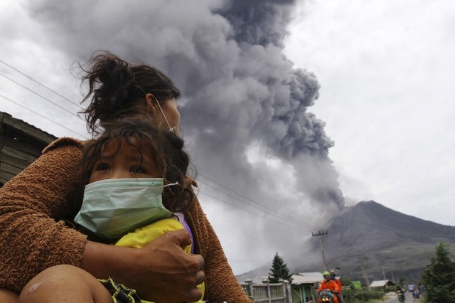 Một bà mẹ con đứng nhìn tro bụi và dung nham phun trào từ núi lửa Sinabung gần ngôi lang Perteguhan, Karo, Indonesia.