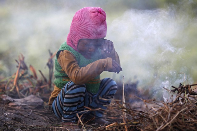 Một cậu bé dụi mắt khi ngồi cạnh đống cỏ khô cháy ở New Delhi, Ấn Độ.