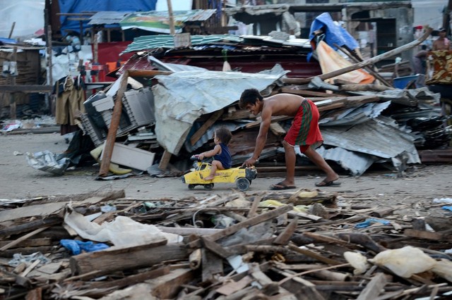 Một người đàn cười rất lạc quan khi chơi với con nhỏ giữa đống nát ở thành phố Tacloban, Philippines.