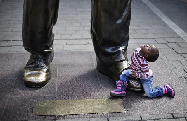 Cậu bé Ndzelo, 3 tuổi, ngồi cạnh bức tượng của cựu tổng thống Nam Phi Nelson Mandela ở thành phố Johannesburg.