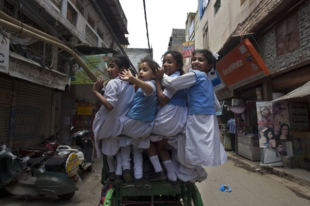 Các nữ sinh vẫy chào khi rời khỏi nhà trên chiếc xe ba bánh để tới trường ở New Delhi, Ấn Độ.