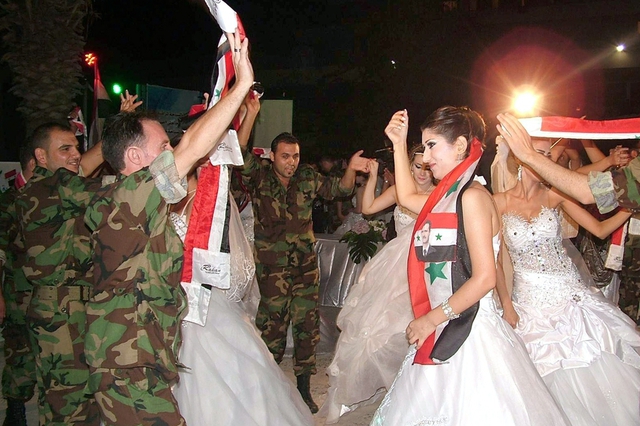 Các binh sĩ chính phủ khiêu vũ với cô dâu của họ trong một lễ cưới tập thể ở Latakia, Syria.