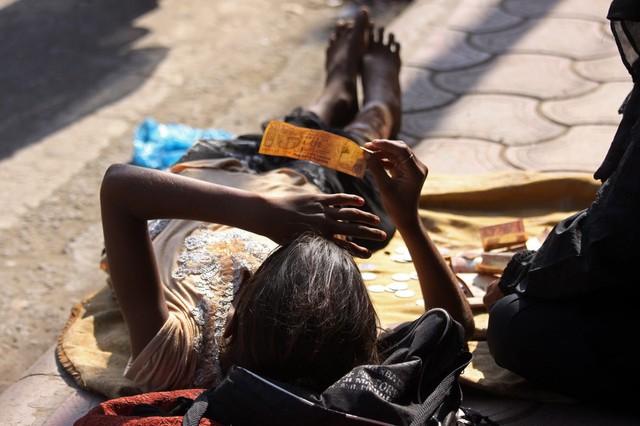 Một bé gái nằm trên đất cầm tờ tiền 10 rupi, trong khi cùng người thân ăn xin trên đường ở Amritsar, Ấn Độ.