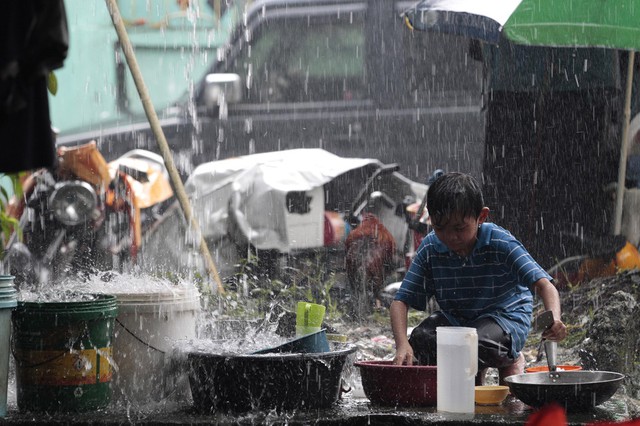 Một cậu bé dùng nước mưa để rửa bát đĩa tại một trung tâm sơ tán lũ lụt ở San Mateo, Philippines.