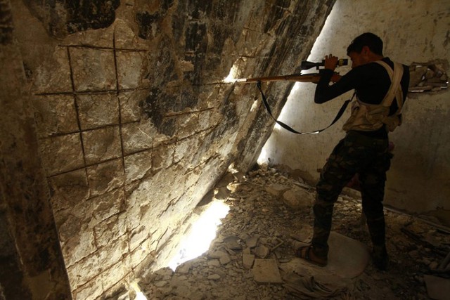 Một chiến binh phiến quân Syria chĩa súng qua một lỗ trên tường trong khi chiến đấu với quân đội chính phủ ở Aleppo, Syria.