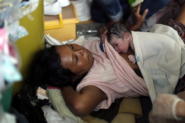 Em bé mới chào đời nằm trên bụng mẹ trong một túp lều tạm tại nhà thờ ở Tacloban, Philippines.