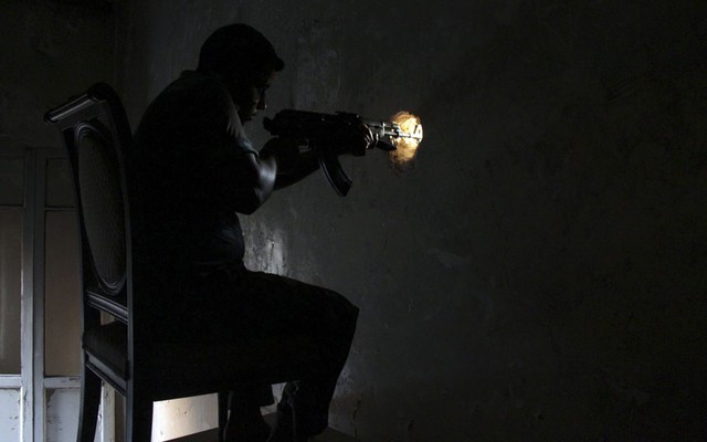 Chiến binh của lực lượng quân đội Syria tự chĩa súng qua một lỗ nhỏ trên tường trong khi giao tranh với quân chính phủ ở Aleppo, Syria.