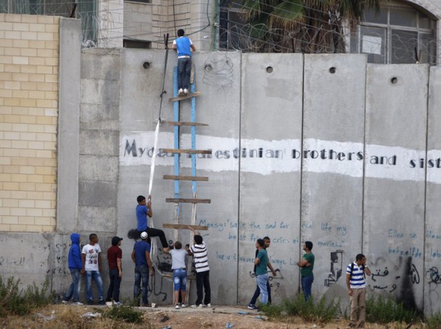 Những người Palestin dùng thang để vượt qua bức tường bê tông làm biên giới ngăn cách với Israel, để tới cầu nguyện tại nhà thờ Al-Aqsa ở Jerusalem trong dịp tháng lễ Ramadan của người Hồi giáo.