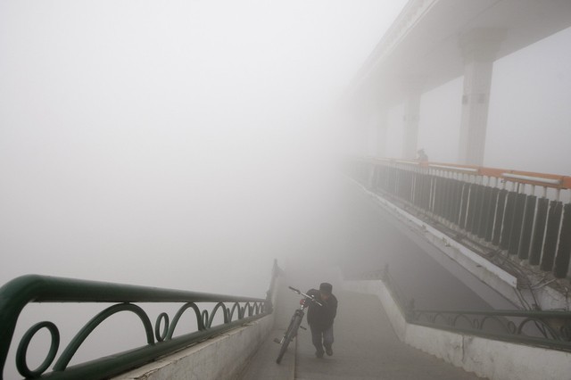 Một người đàn ông dắt xe đạp lên cầu dành cho người đi bộ dưới sương sớm mù mịt ở thành phố Cáp Nhĩ Tân, Trung Quốc.