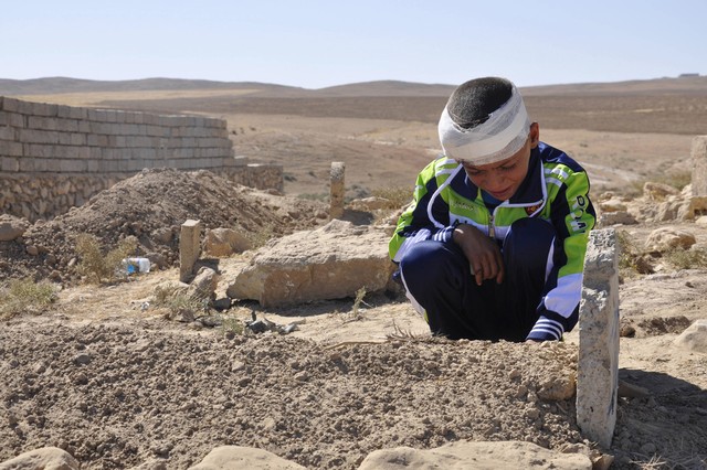 Cậu bé Mohammed Moses với vết thương ở đầu ngồi khóc bên mộ bố bị chết trong một vụ đánh bom tự sát ở Qabak, Iraq.