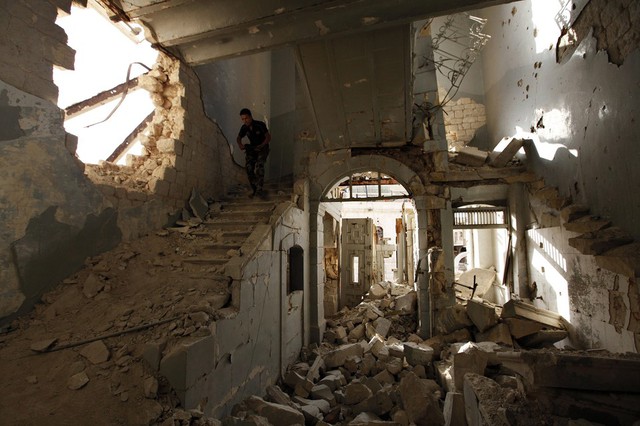 Chiến binh phiên quân cầm súng đi xuống cầu thang trong một ngôi nhà đổ nát ở thành phố Aleppo, Syria.