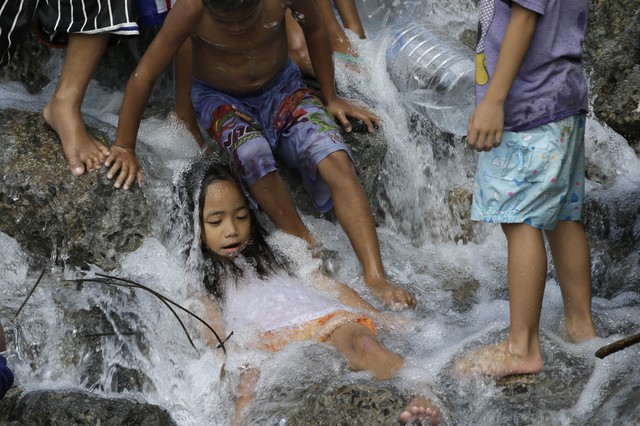 Trẻ em thích thú tắm dưới dòng nước chảy ra từ đường ống nước bị vỡ ở thành phố Quezon, Philippines.