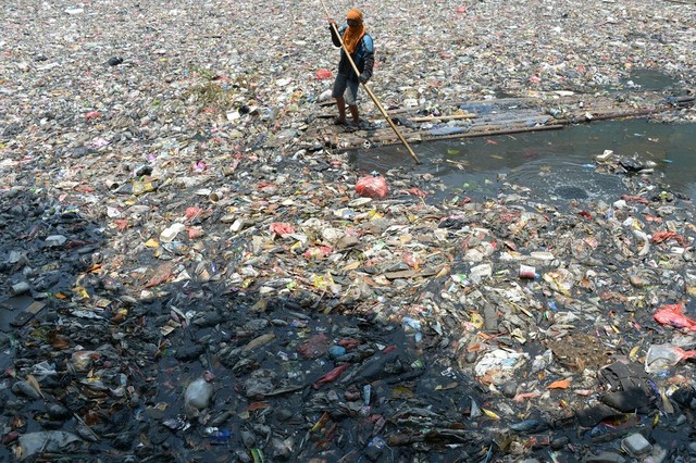 Một công nhân vệ sinh chèo bè  trên dòng sông đầy rác ở Jakarta, Indonesia.