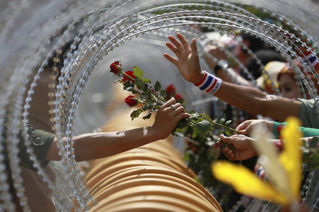 Những người biểu tình chống chính phủ đưa hoa hồng qua hàng rào dây thép gai cho một binh sĩ Thái Lan ở thủ đô Bangkok.