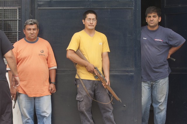 Những người chủ cầm súng đứng trước cửa hàng để ngăn chặn những kẻ cướp bóc và hôi của ở San Miguel de Tucumán, Argentina. Tình trạng cướp bóc gia tăng sau khi cảnh sát đình công đòi tăng lương.