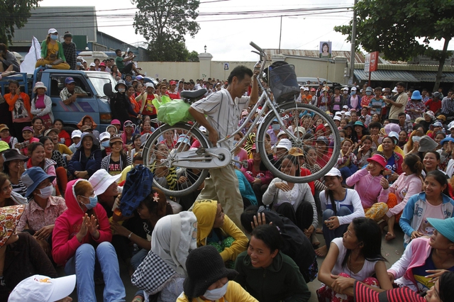 Một người đàn ông vác xe đạp qua một đường phố với đầy các công nhân may đang ngồi biểu tình đòi tăng lương ở Phnom Penh, Campuchia.