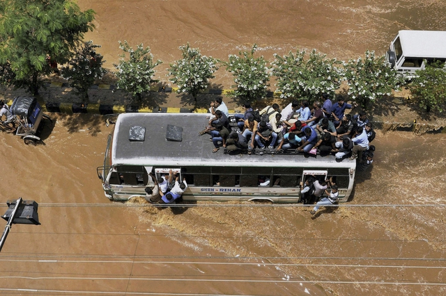 Xe bus chở quá tài di chuyển trên đường phố ngập nước sau một trận mưa lớn ở Gauhati, Ấn Độ.