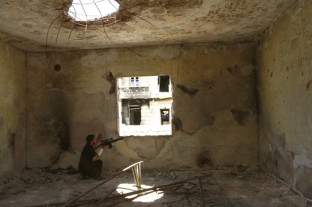 Một chiến binh của lực lượng quân đội Syria tự do kề súng lên cửa sổ từ trong một ngôi nhà đổ nát ở thành phố Aleppo, Syria.