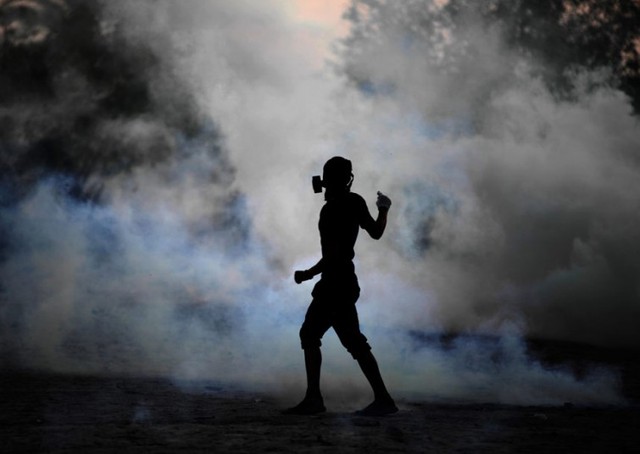 Người biểu tình chống chính phủ đeo mặt lạ phòng khí độc đứng giữ màn khói hơi cay do cảnh sát phóng ra tại ngôi làng Shakhura, Bahrain.