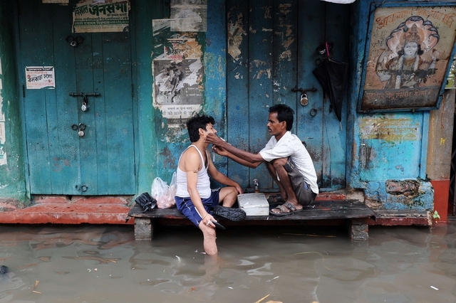 Thợ cắt tóc cạo râu cho khách hàng ngay trên đường phố ngập lụt ở Kolkata, Ấn Độ.