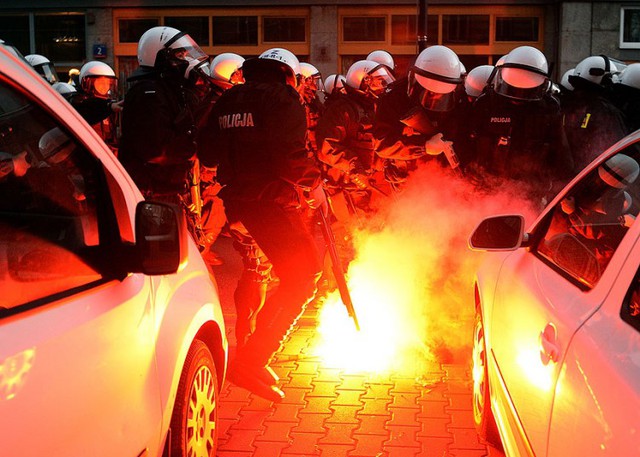 Cảnh sát chống bạo động cố gắng dập tắt pháo sáng do những người biểu tình ném ở Ba Lan.