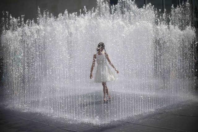 Thiếu nữ chơi đùa giữa đài phun nước dưới trời nắng nóng ở thủ đô London, Anh.