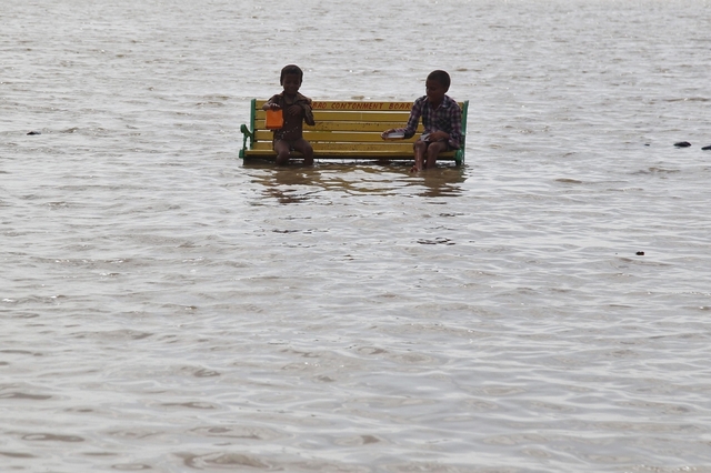 Hai cậu bé ngồi chơi trên ghế bên bờ sông Hằng bị ngập lụt ở Allahabad, Ấn Độ.